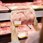 Mulher no mercado escolhendo bandeja de frango no supermercado.