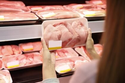 Mulher no mercado escolhendo bandeja de frango no supermercado.