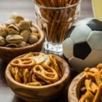 Imagem de petiscos em potes pequenos em cima de uma mesa com uma bola de futebol e um copa grande de refrigerante