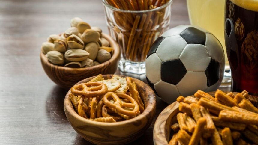 Imagem de petiscos em potes pequenos em cima de uma mesa com uma bola de futebol e um copa grande de refrigerante