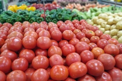 Foto mostra vários tomates vermelhos empilhados na gôndola do supermercado.