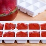 Imagem de uma forma de gelo branca com molho de tomate dentro dos quadradinhos