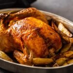 Foto mostra um frango inteiro assado dentro de uma forma em cima de uma mesa.