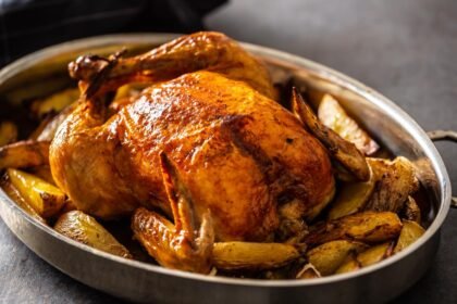 Foto mostra um frango inteiro assado dentro de uma forma em cima de uma mesa.