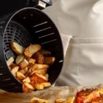 Imagem de uma pessoa tirando batatas do cesto de uma air fryer